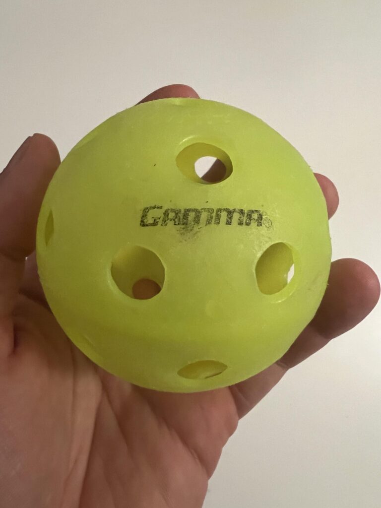 Close-up of a used green Gamma Photon indoor pickleball showing logo, holes and surface wear