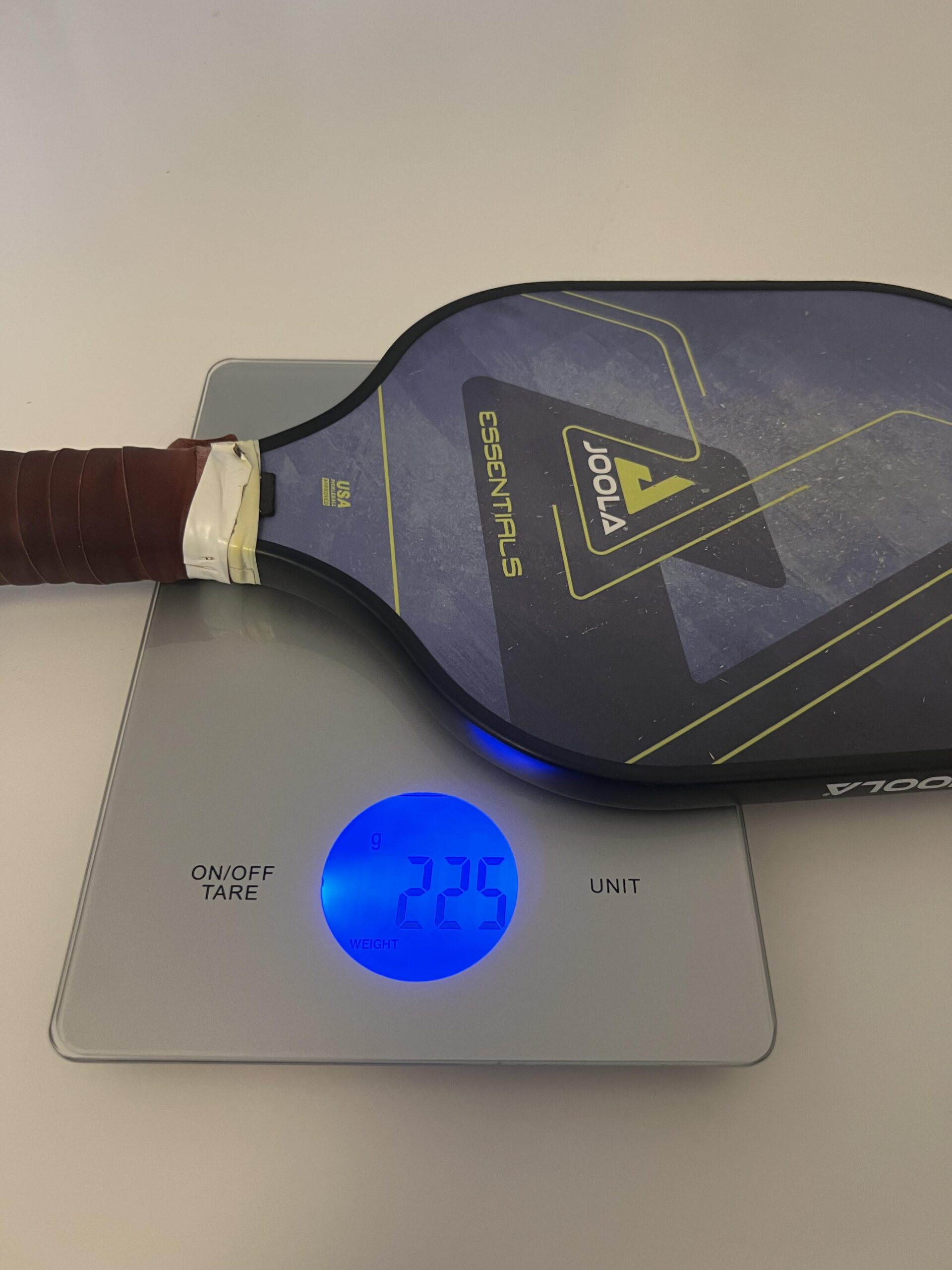 Raquete JOOLA Essentials na balança digital marcando 225 gramas com overgrip