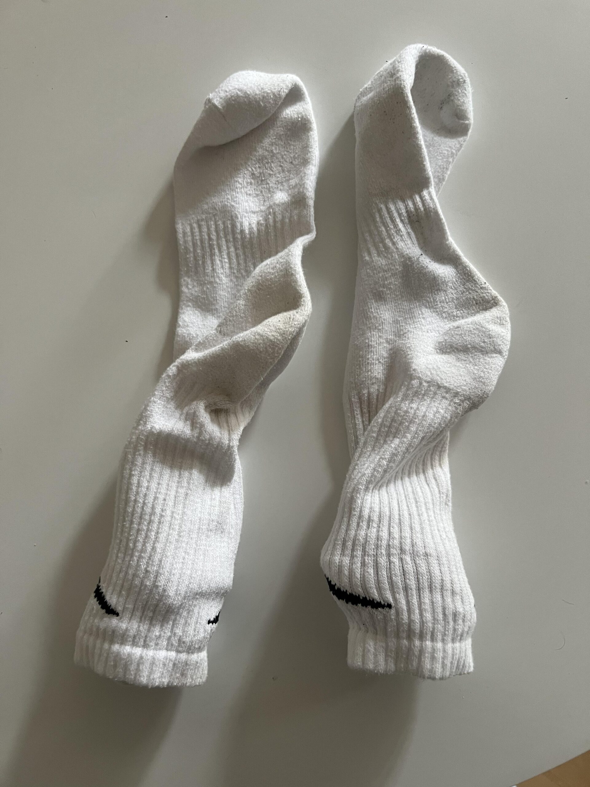 Reverse sides of two used white Nike Everyday Cushioned socks showing their knit